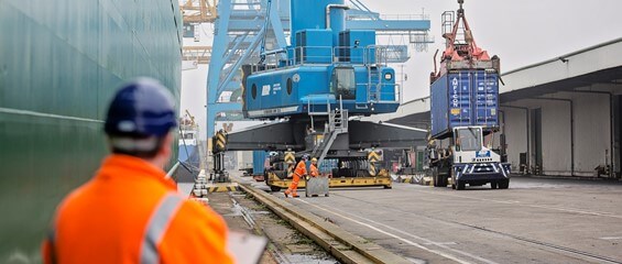A port worker in PPE overseeing a crane operation